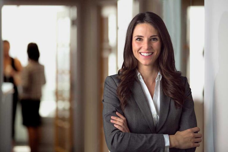 A person in professional attire speaks with a concerned individual across a table in a warmly lit office.